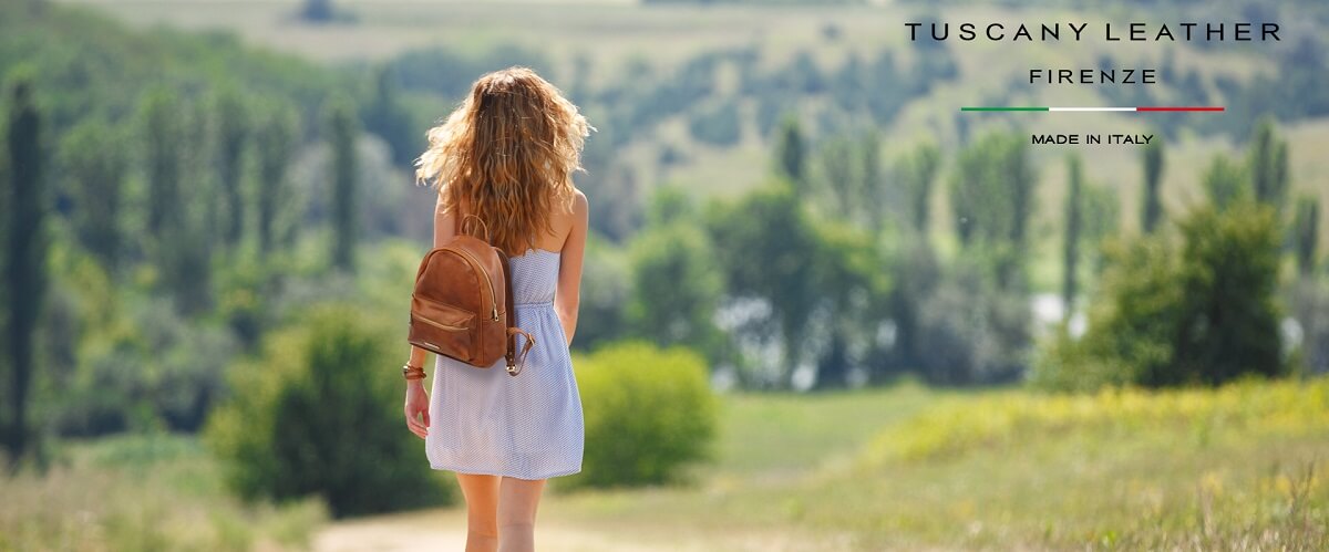 Woman carrying a small tan leather backpack in a green landscape